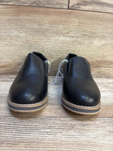 Pair of black slip-on kids dress shoes with tan soles on wooden floor