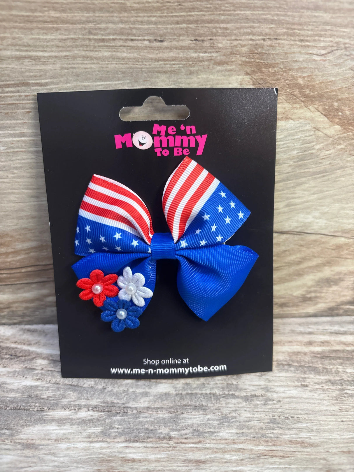 Front of Fourth of July hair bow showing flag-print ribbon, blue bow, and red white blue flower accents on black card
