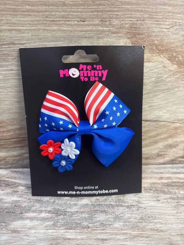 Front of Fourth of July hair bow showing flag-print ribbon, blue bow, and red white blue flower accents on black card