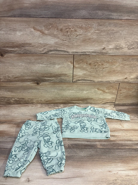 Flat lay of 2-piece Disney Baby green sweatshirt and joggers showcasing all-over Mickey Mouse sketch print and ‘MICKEY’ chest lettering on wood background