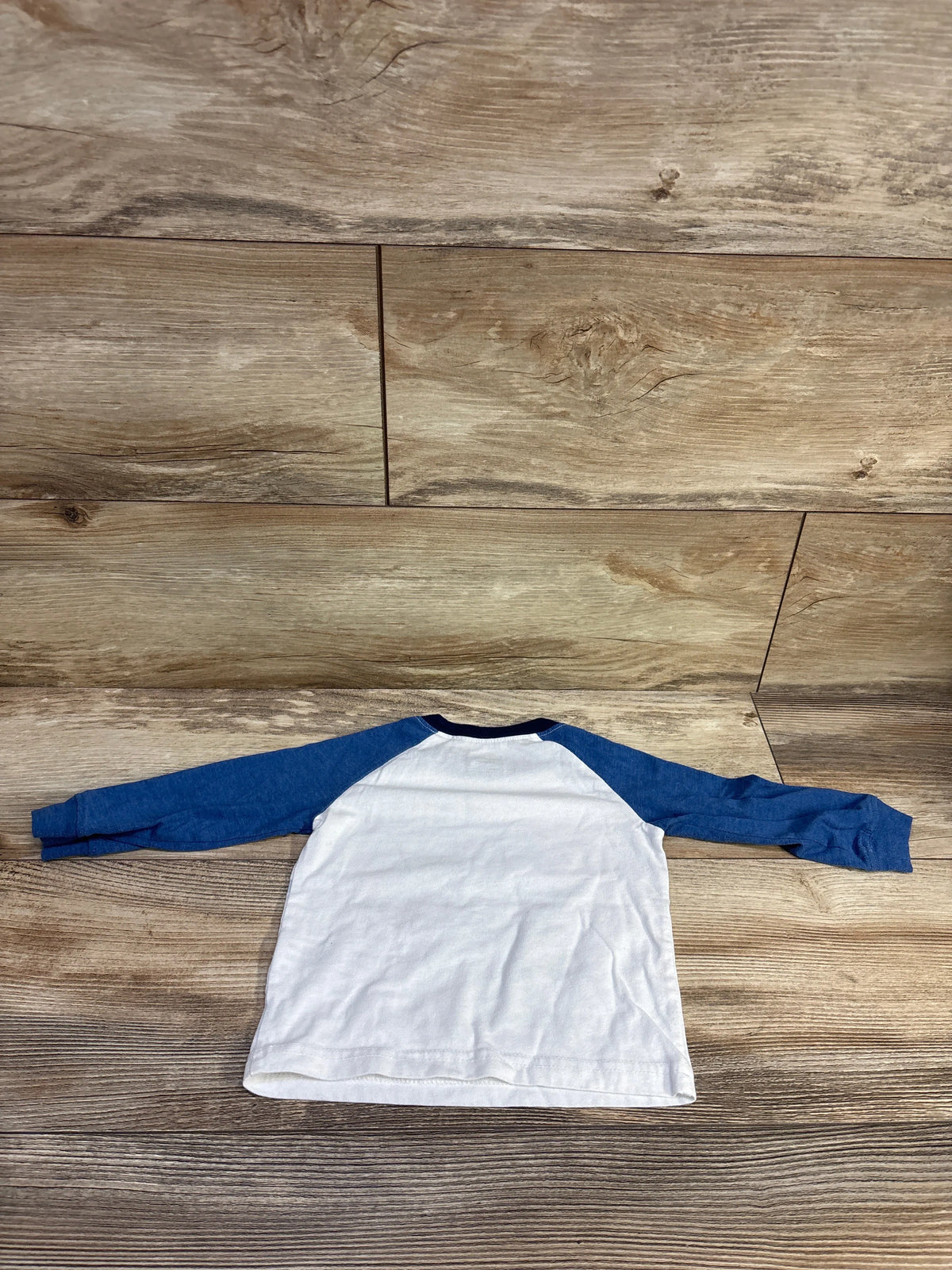 Top view of Carter’s football shirt in white with blue long sleeves laid flat on a wood floor