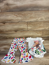 Flat lay of 2-piece baby set 18-24 mo: white bodysuit with giraffe graphic and colorful flared ruffle pants on wood floor