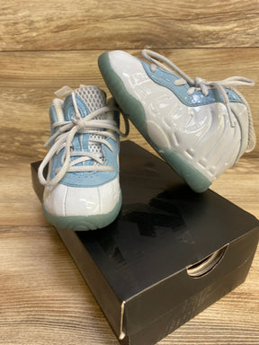 Angled view of Nike Little Posite One toddler sneaker with glossy white and blue upper and translucent sole on shoebox