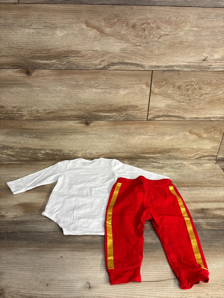 White long-sleeve baby onesie with red pants featuring gold side stripes, laid on wood floor