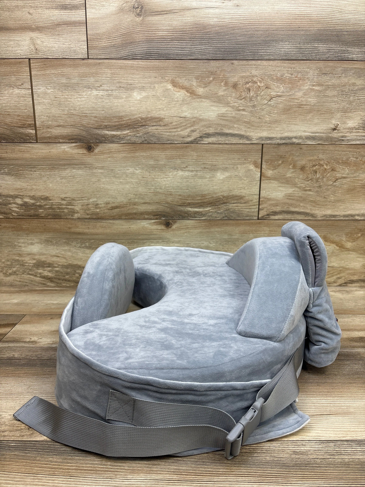 Front three-quarter view of Momcozy CozyPro nursing pillow in grey showcasing waist strap and buckle on a wood background