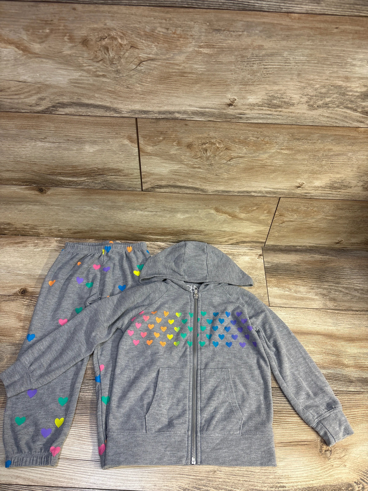 Top view of Chaser Kids 2pc gray zip-up hoodie and joggers set, size 4T, showcasing rainbow heart prints on a wood floor