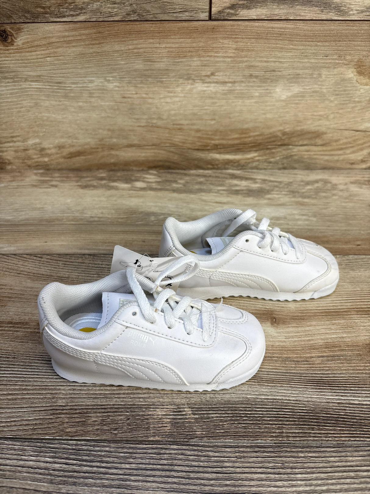 White Puma kids sneakers with laces on wood background, gently used children's shoes