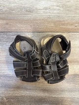 Brown leather toddler sandals with white stitching on wood floor