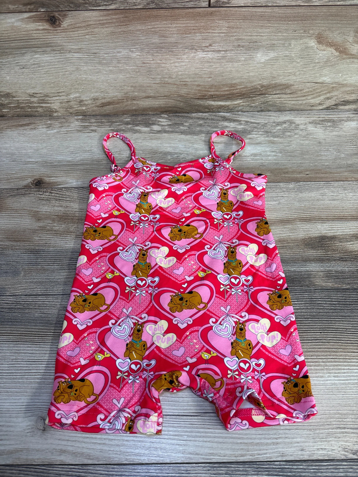 Flat lay of pink Shein x Scooby-Doo shortie romper showing spaghetti straps and all-over heart and Scooby-Doo print on wood plank background