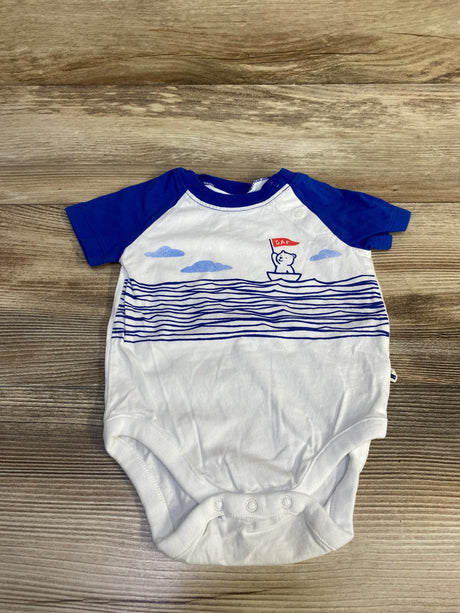 Front flat-lay of white Baby Gap bodysuit with blue raglan sleeves, blue wave stripes and bear-in-boat graphic on wood
