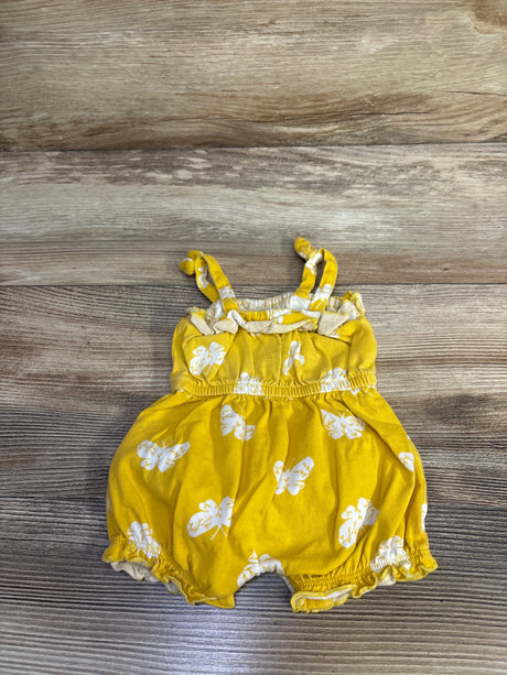 Flat lay newborn yellow shortie romper with white floral print, knotted straps, elastic waist, ruffled legs on wood floor