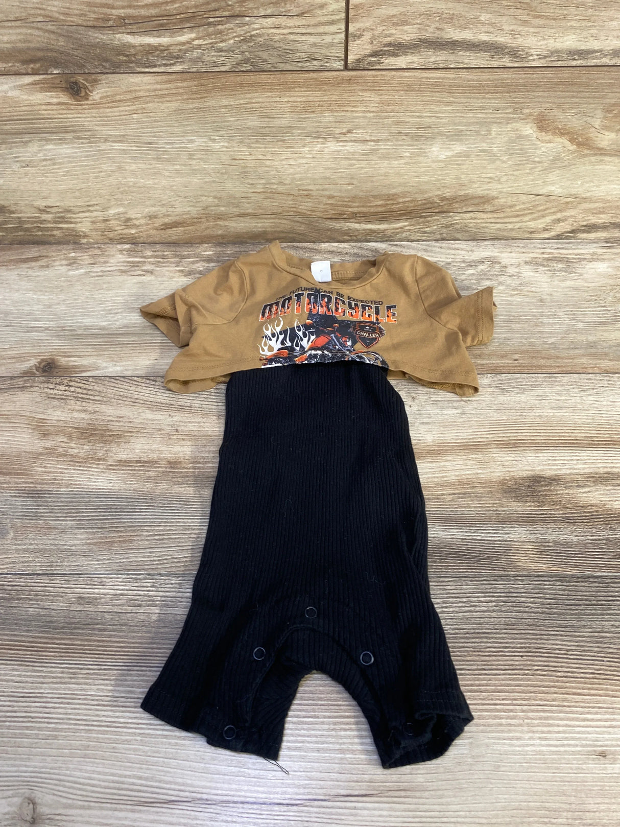 Flat lay of two-piece baby set brown cropped motorcycle tee and black ribbed romper with snap crotch on wood background