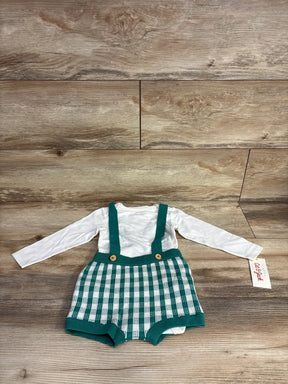 White long-sleeve baby bodysuit with green and white checkered knit suspender shorts on wooden floor