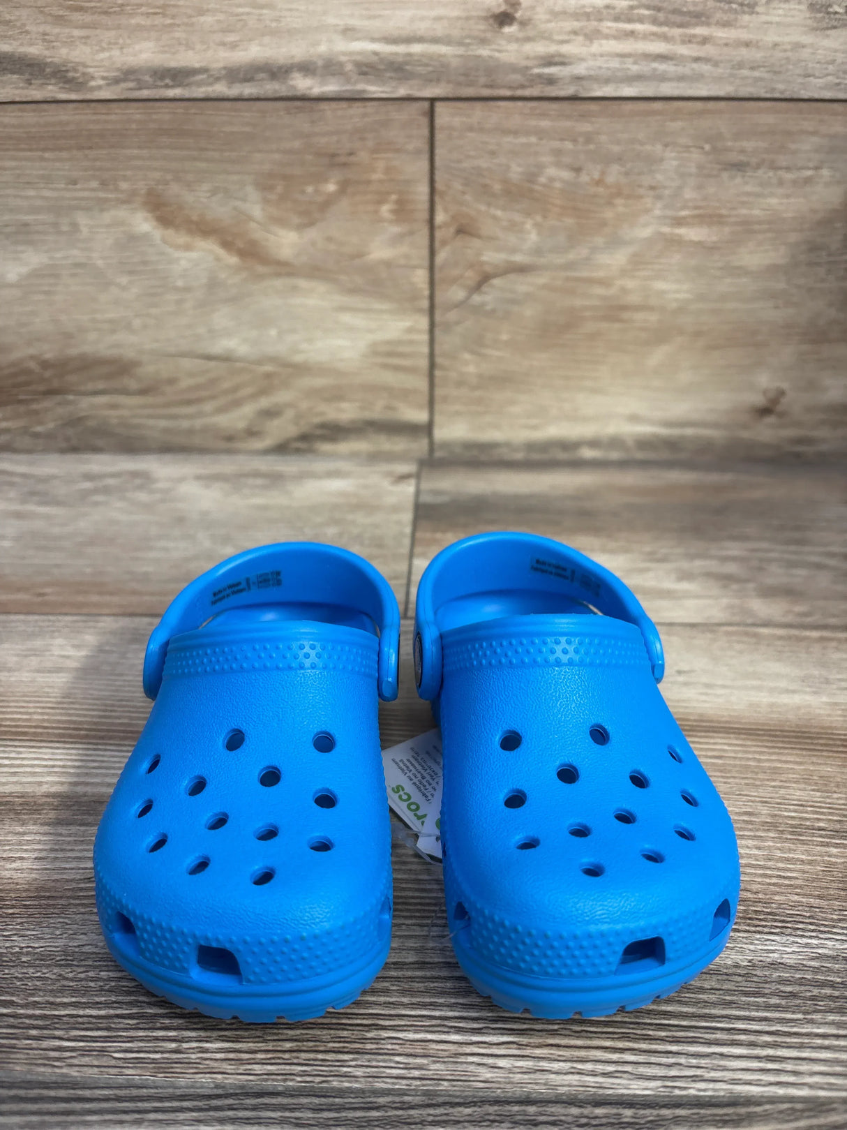 Front view of kids' Crocs Classic clogs size 7C showing ventilation holes and heel strap on wood floor background