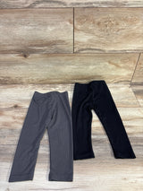 Flat lay of two ribbed baby leggings showing elastic waist and ribbed texture, black and charcoal on wood background