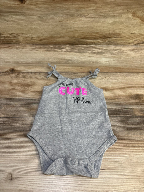 Flat lay of grey baby bodysuit with tie shoulder straps and snap crotch, pink 'CUTE' text on wood background