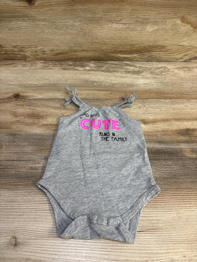 Flat lay of grey baby bodysuit with tie shoulder straps and snap crotch, pink 'CUTE' text on wood background