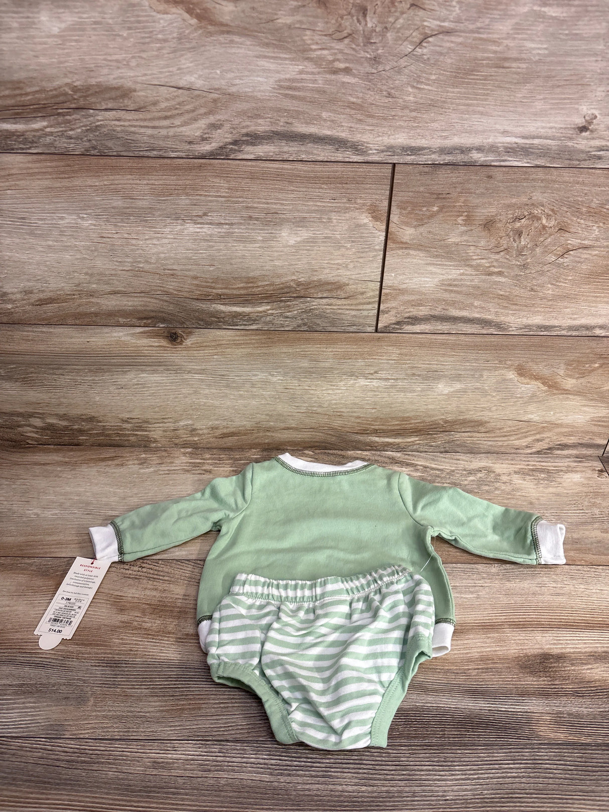 Newborn green long-sleeve shirt and striped diaper cover set on wooden floor, baby clothes with price tag