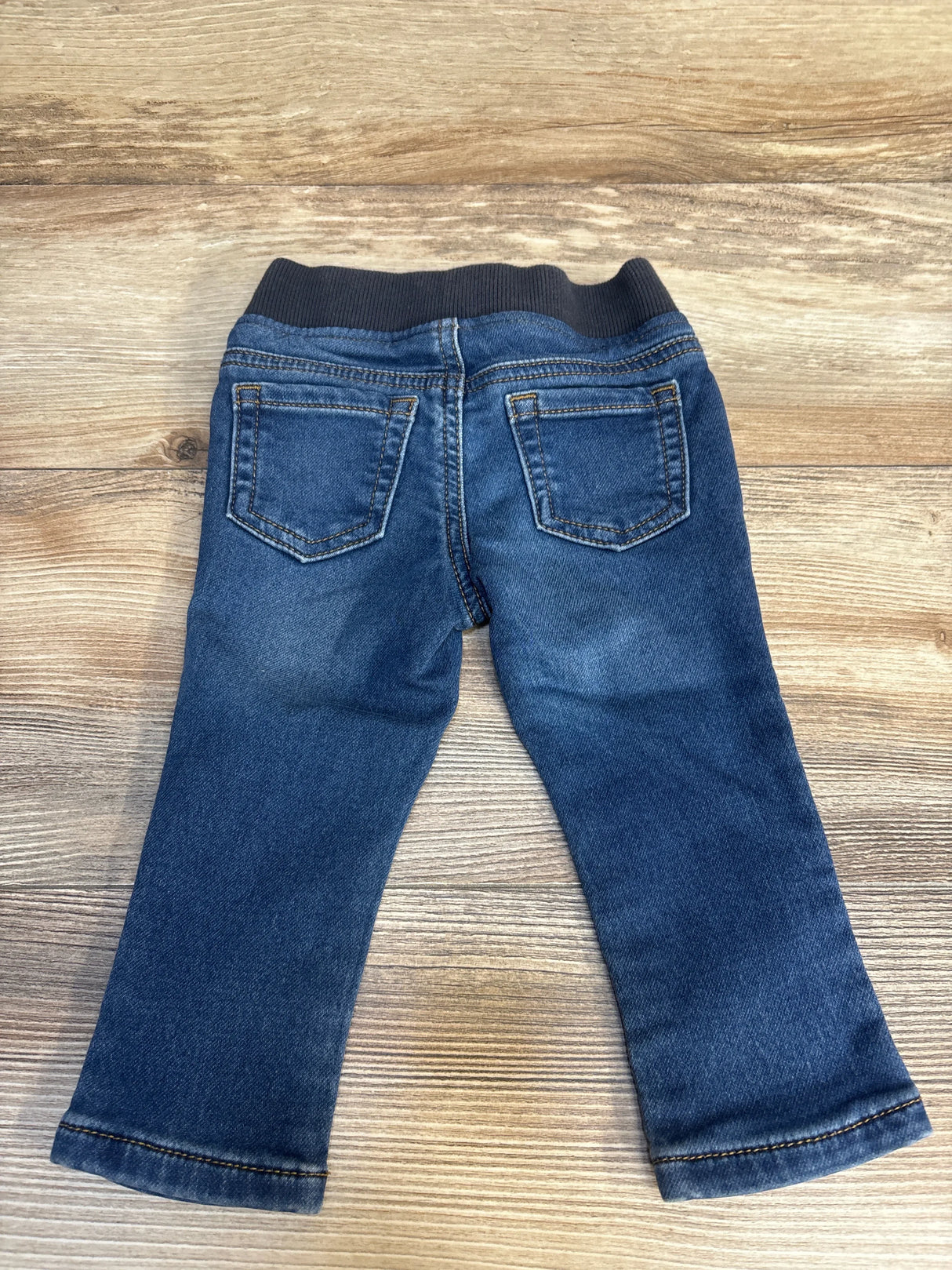 Back view of baby jeans with elastic waistband and back pockets laid flat on wood plank background