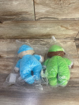 Top-down view of two Lakeshore washable cuddly baby dolls, one blue and one green, in plastic bags on wood floor