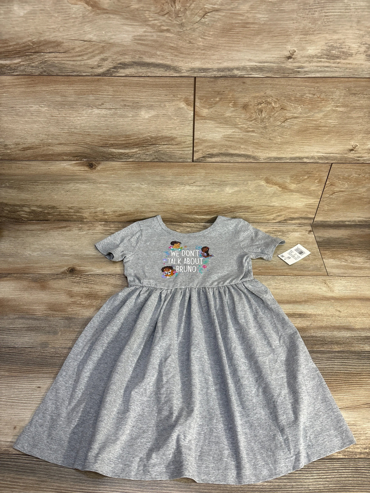 Flat-lay of grey Disney girls dress 5T with short sleeves and chest print We Don't Talk About Bruno on wood background
