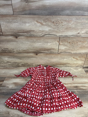 Red and white geometric pattern baby dress with puff sleeves, laid on wood floor