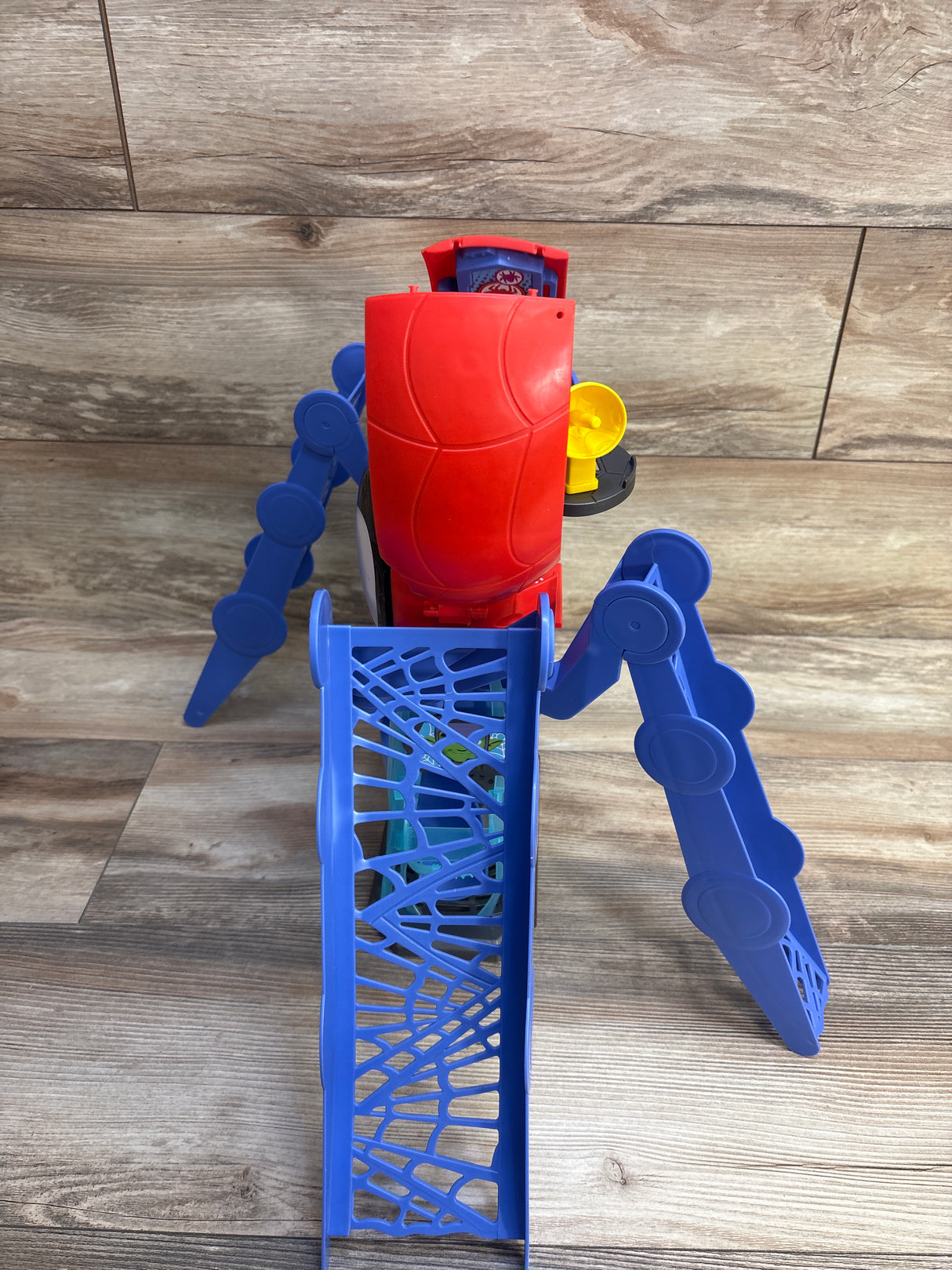 Angled top view of Hasbro Spidey playset showing red cockpit, blue web ramp and articulated legs on wood floor