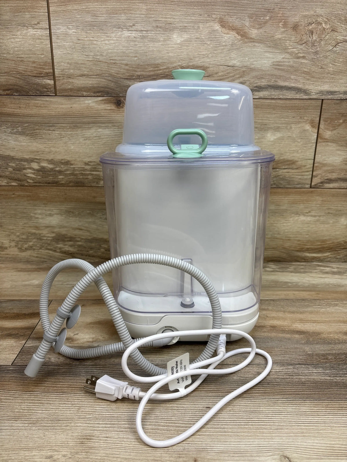 Front view of Momcozy KleanPal Pro baby bottle washer, sterilizer and dryer showcasing clear chamber, hoses and power cord on a wood surface