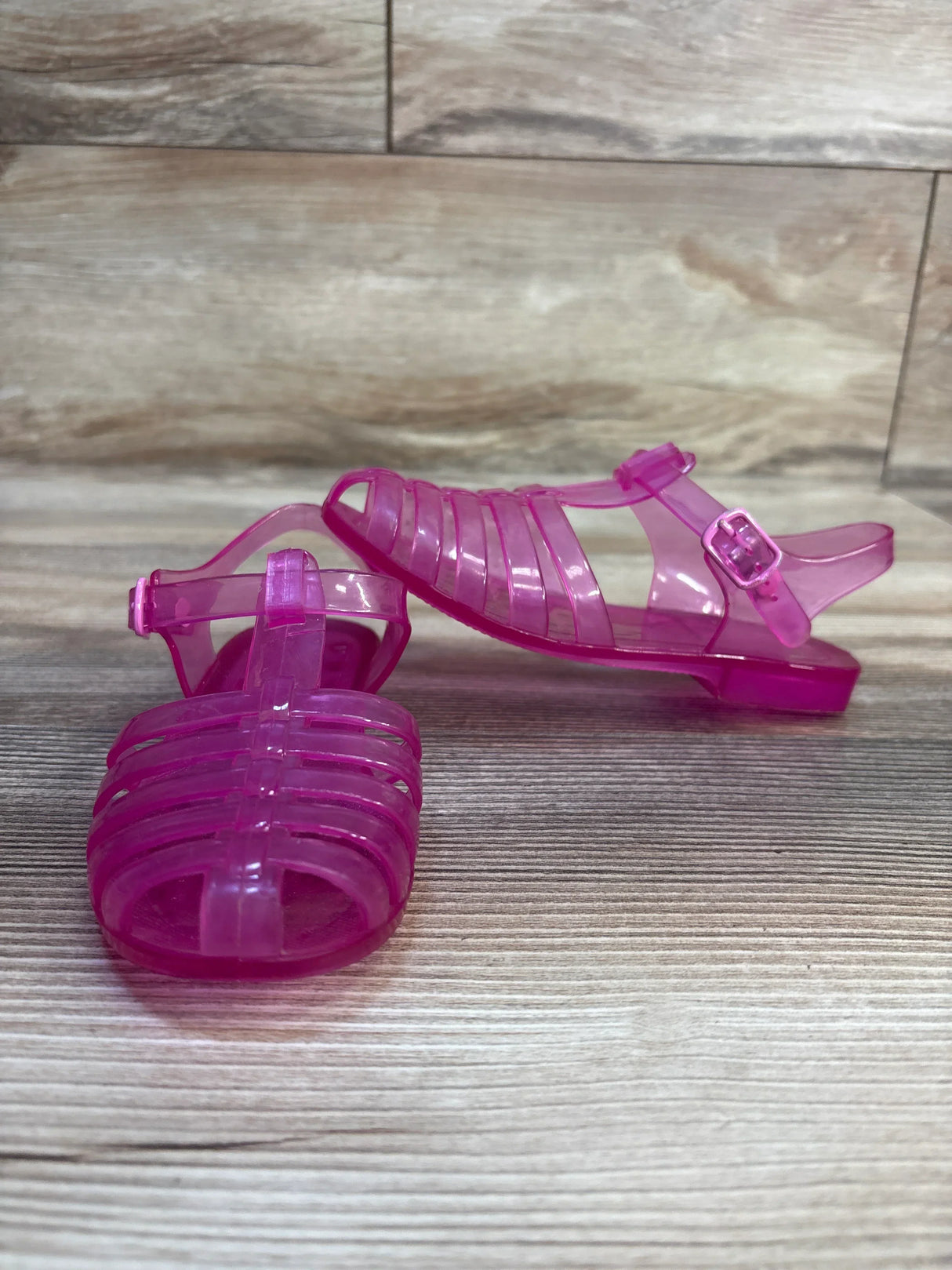 Pink jelly sandals for kids with buckle straps on wood floor background