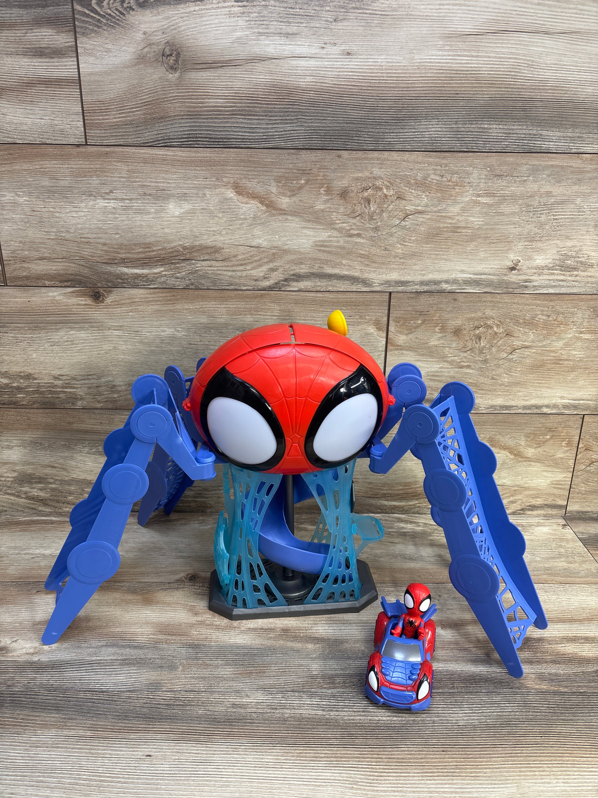 Front of Hasbro Spidey Web-Quarters playset with red spider head, blue legs, spiral slide and small car on wood floor