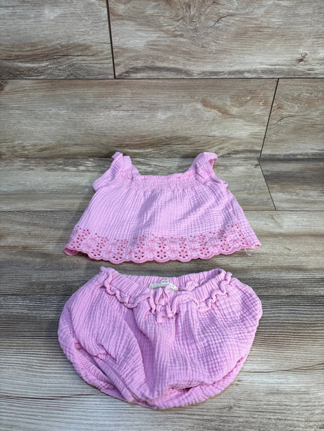 Pink baby girl two-piece outfit with eyelet trim top and ruffled shorts, laid on wood floor