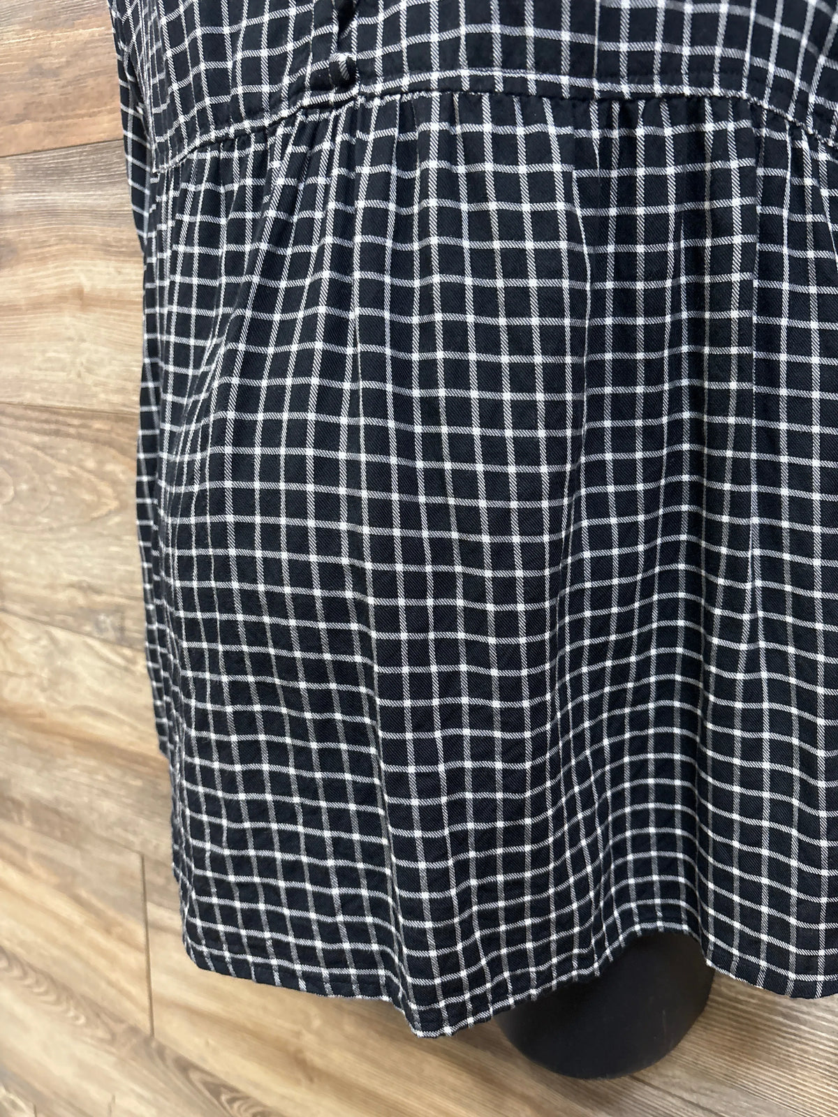 Close-up of black and white plaid maternity flannel popover tunic showing gathered waist and hem on a wood floor