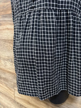 Close-up of black and white plaid maternity flannel popover tunic showing gathered waist and hem on a wood floor