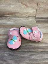 Angled front view of pink PU baby sneakers with blue butterfly and heart patches and black stitched sole on wood floor