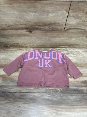 Kids mauve long sleeve shirt with 'London UK' text in pink and blue, laid on wood floor