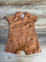 Rust-colored baby romper with sun pattern, short sleeves, and front buttons on wood background.