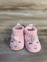 Pink knit baby booties with unicorn horns, ears, and smiling faces on wood floor