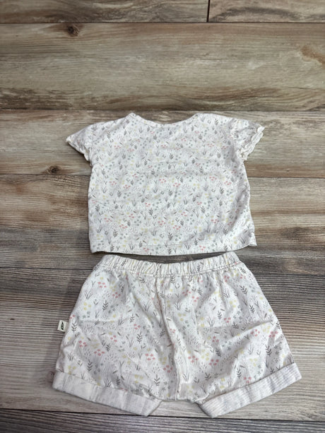Top-down view of ivory organic two-piece shirt and shorts set with floral print and ruffled sleeves on a wood surface