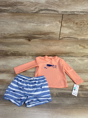 Flat lay of coral long sleeve rash guard with whale graphic and matching blue and white striped swim shorts on wood background