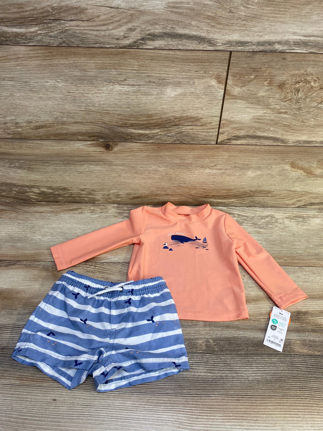 Flat lay of coral long sleeve rash guard with whale graphic and matching blue and white striped swim shorts on wood background
