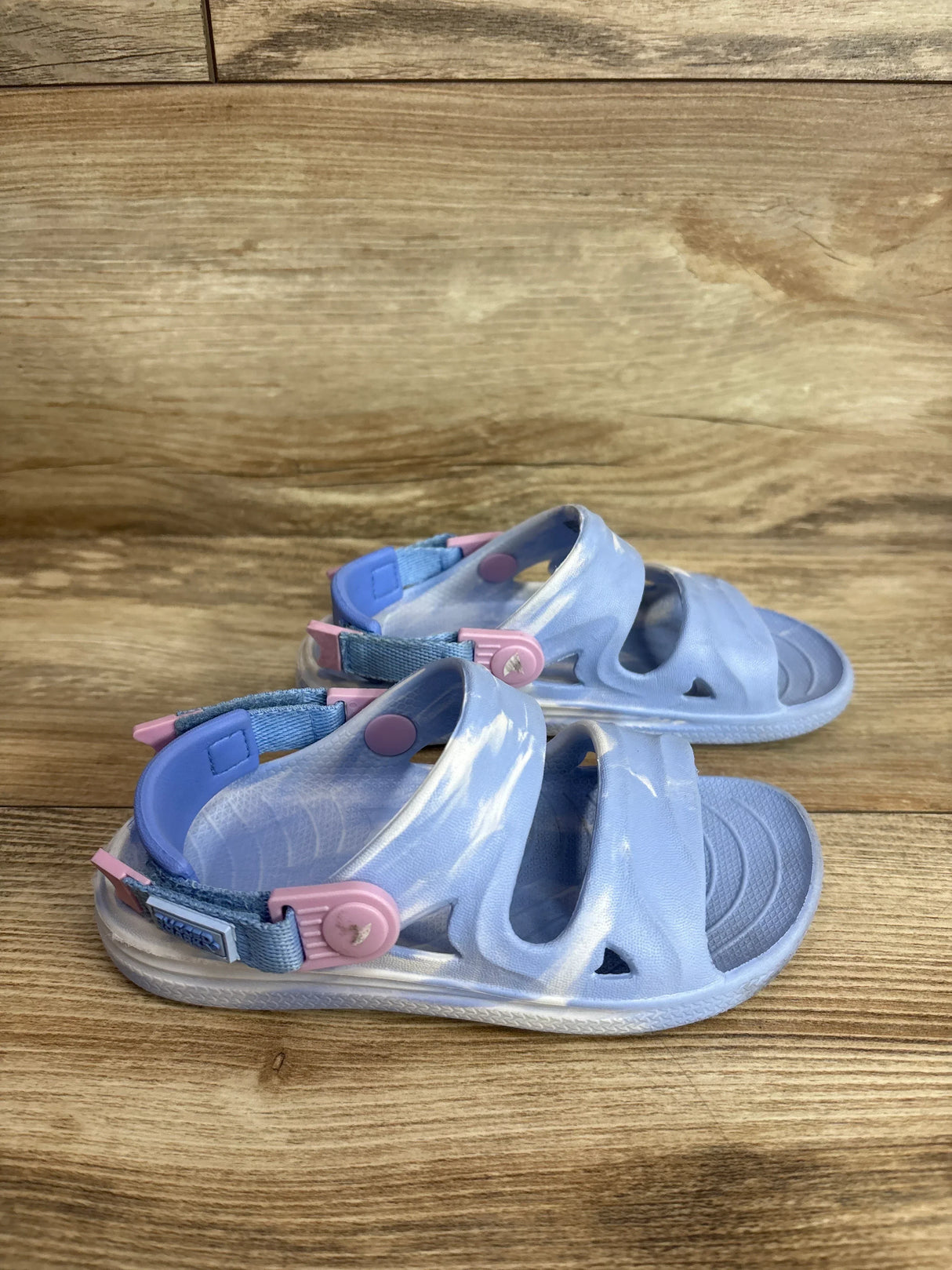 Side view of blue Rugged Shark Nature sandals size 10C showing two straps and pink heel tabs on wood floor