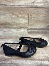 Side view of Cat & Jack Nora toddler black slip-on ballet flats showing elastic strap, bow detail, and low heel on wood floor background
