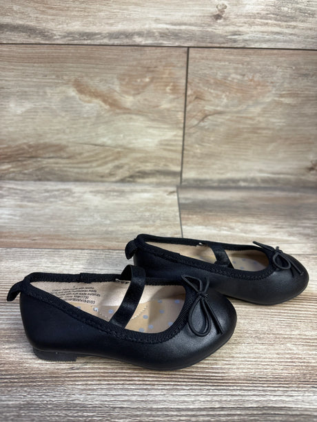 Side view of Cat & Jack Nora toddler black slip-on ballet flats showing elastic strap, bow detail, and low heel on wood floor background