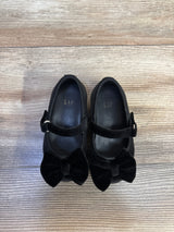 Top-down view of Baby Gap velvet Mary Jane flats showcasing velvet bows and a buckle strap on light wood floor