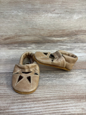 Front and side view of newborn tan leather soft-sole moccasins showing star cutout and white stitching on wood background