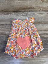 Flat lay of baby shortie romper showcasing large pink heart patch and orange-pink floral print with wood background