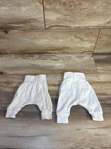 Two pairs of baby harem pants in white and off-white, soft cotton, laid on wood floor for resale