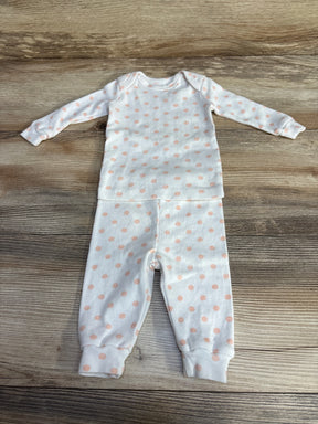 Flat lay of white 2-piece baby pajama set showcasing light peach polka dots and cuffed ankles on a wood background