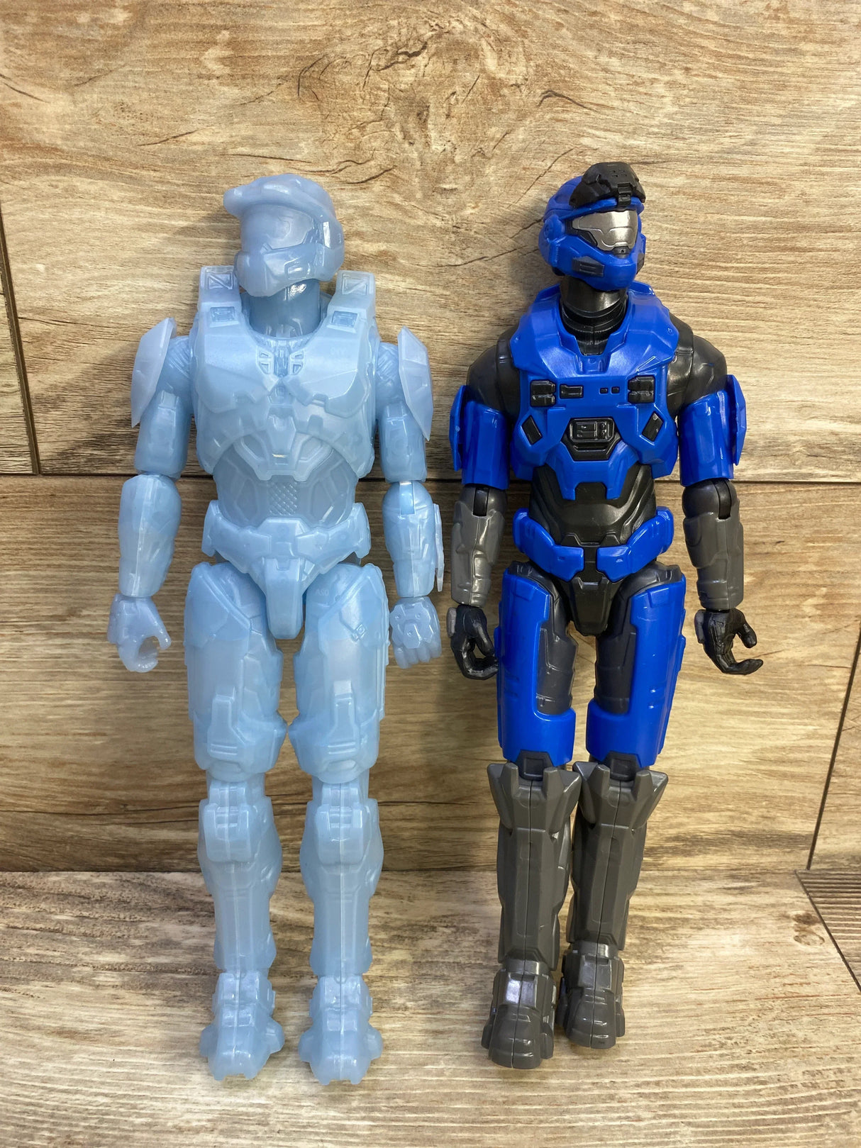 Front view of two 12-inch Halo Spartan figures: light-blue active camo and blue-gray Master Chief on wood background