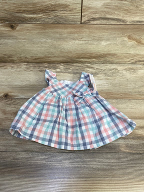 Top-down flat-lay of newborn plaid baby dress showcasing pastel pink, mint, and gray check pattern with ruffle sleeves and side bow on wood background